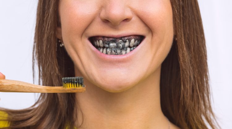 Woman brushing teeth with charcoal toothpaste, showing black-stained smile – Downtown Plaza Dental, Sacramento, CA.