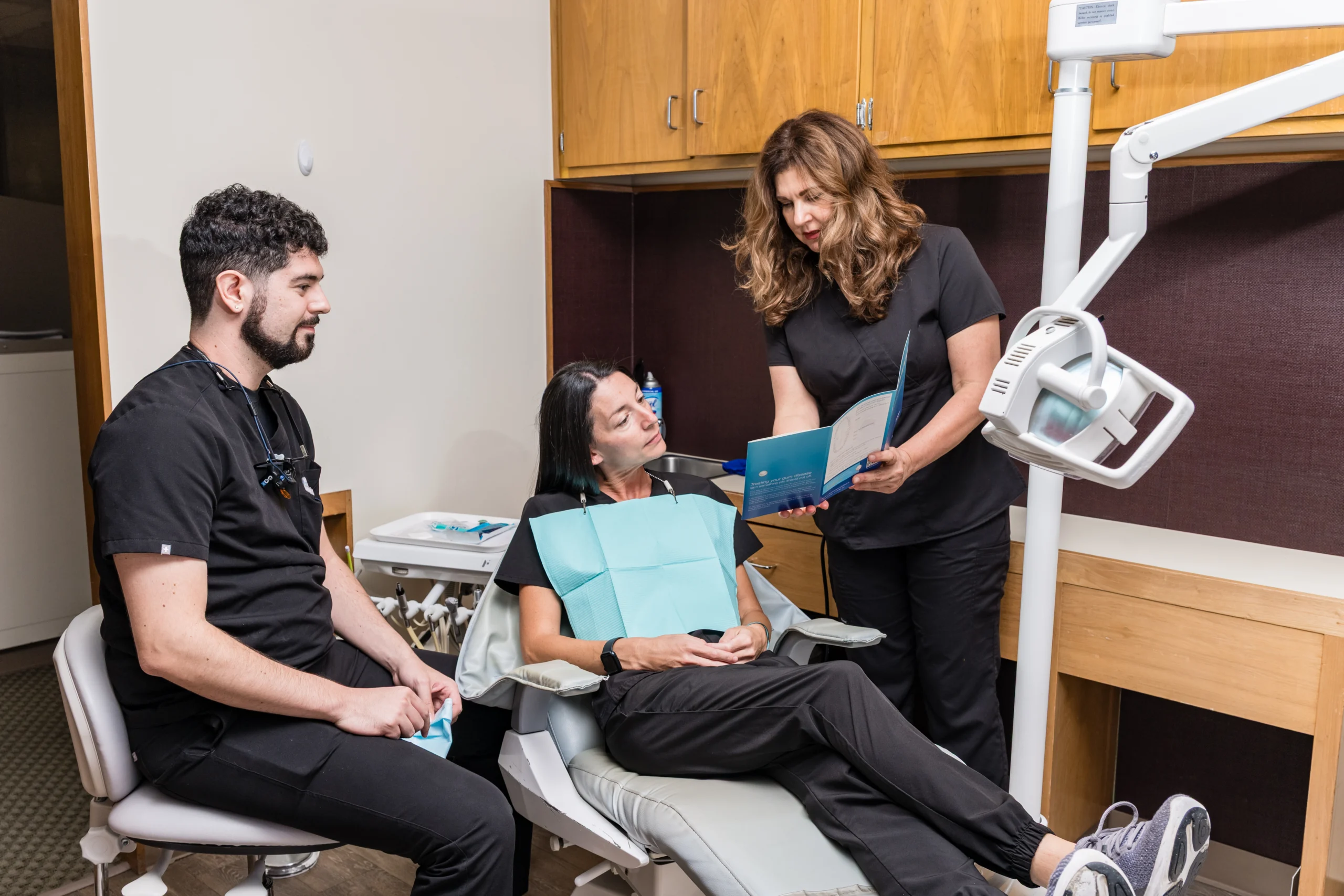 Dental professionals discuss care with a patient seated in a dental chair.