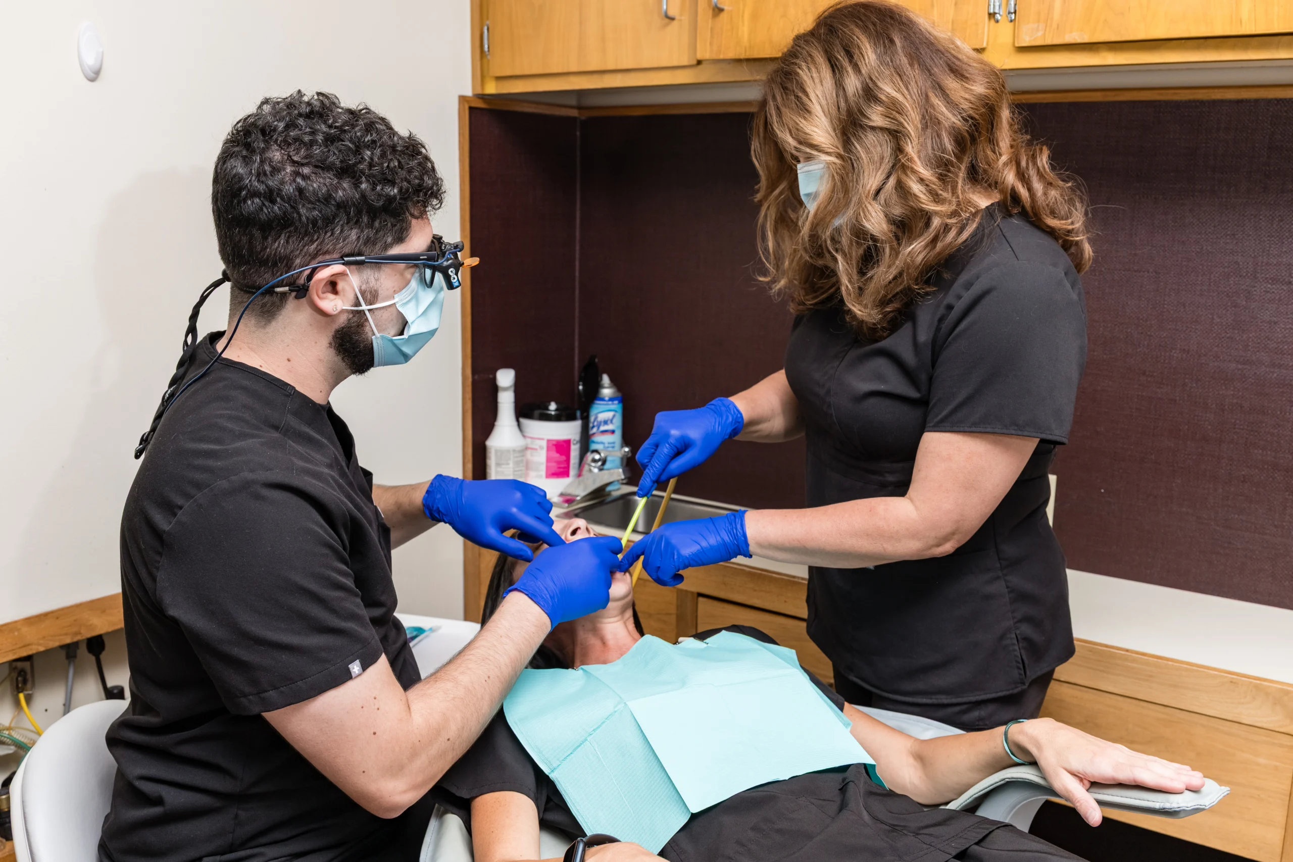 Dental professionals wearing masks and gloves treat a patient in a dental chair.